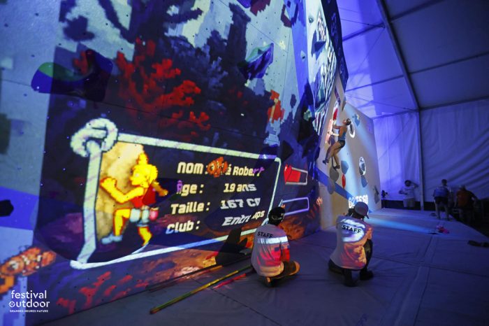 Participants escaladant un bloc d’escalade avec des projections lumineuses. Mapping avec le nom de la grimpeuse, sa taille, son age et son club