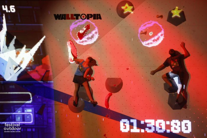 Participants escaladant un bloc d’escalade avec des projections lumineuses. Lumière rouge avec un chrono blanc